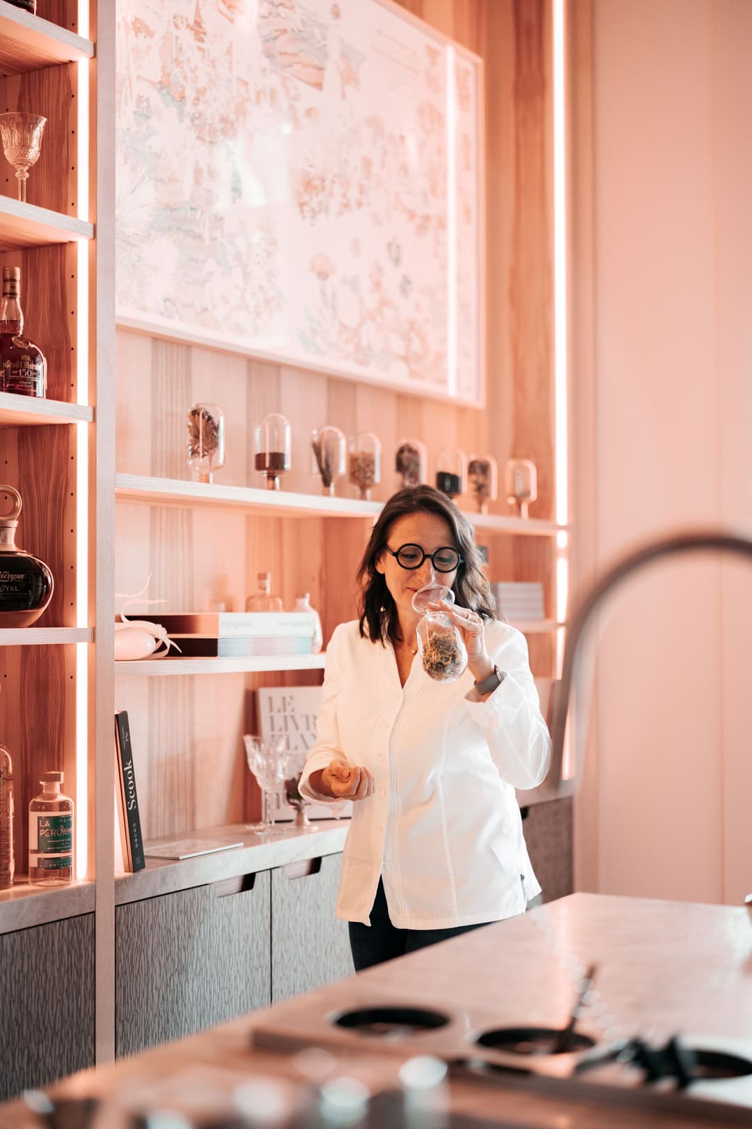Femme en blazer blanc devant une vitrine illuminée rose pêche affichant des montres et accessoires de luxe