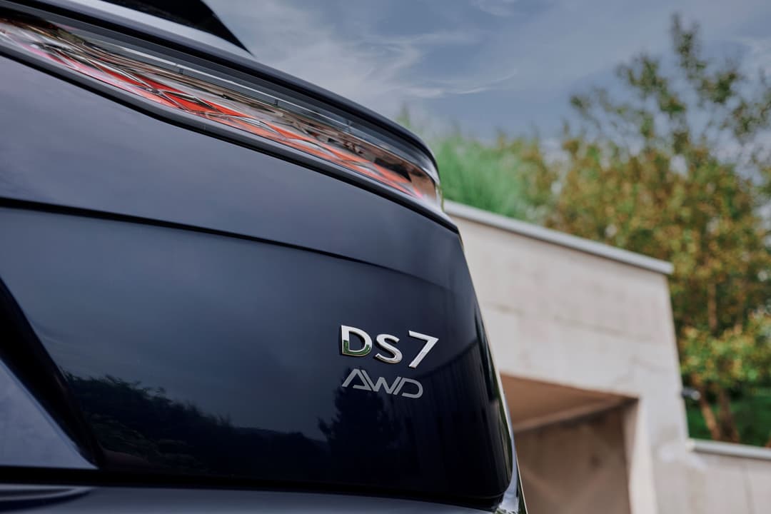 Détail du hayon arrière d'une DS 7 noire avec inscription DS7 AWD et feu arrière, garée devant une maison