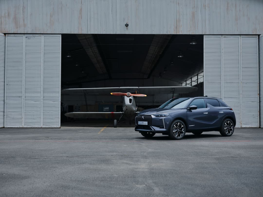 DS 3 Étoile bleu foncé avec jantes Toulouse devant un hangar contenant un avion vintage