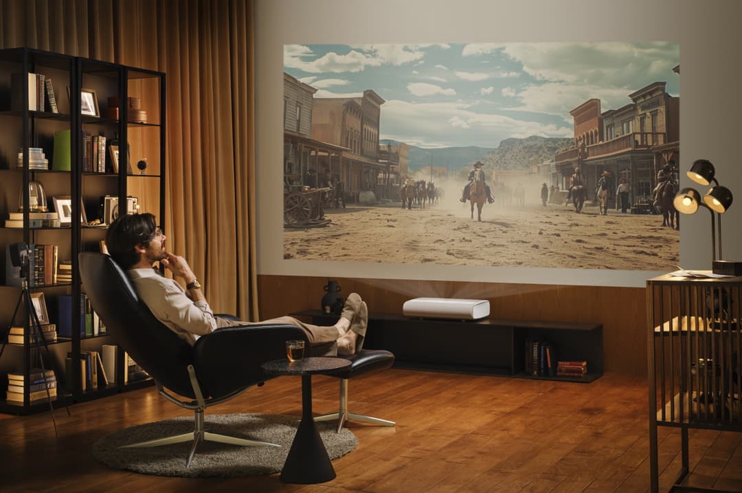 Projecteur Samsung The Premiere affichant un film western sur un mur de salon élégant, un homme assis dans un fauteuil regardant l'écran géant