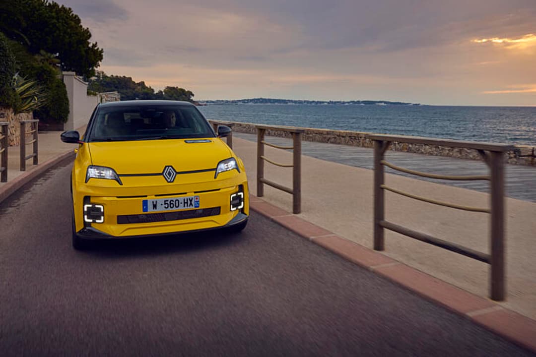 Renault 5 E-Tech jaune vif garée sur une promenade côtière avec vue sur la mer au coucher du soleil