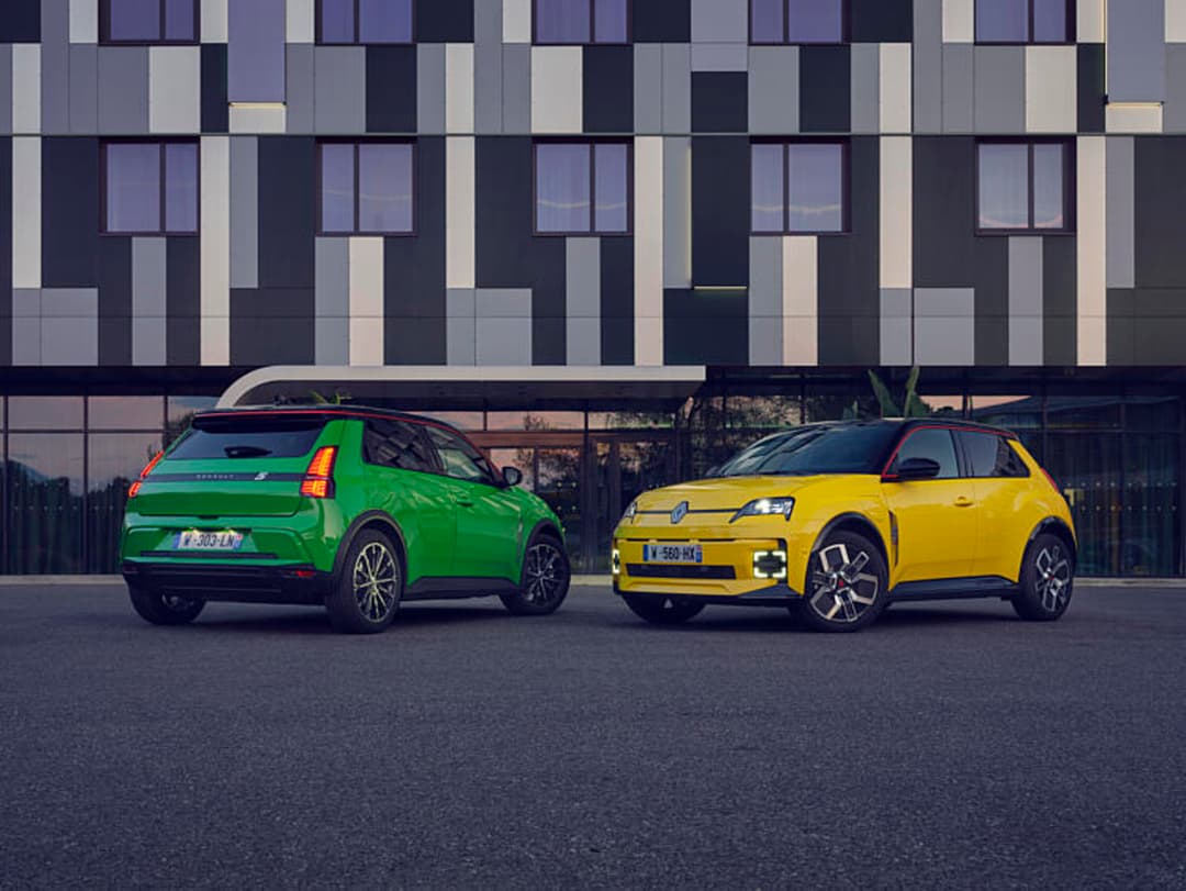 Deux Renault 5 E-Tech 100% electric, une verte et une jaune, stationnées côte à côte devant un immeuble moderne aux façades géométriques