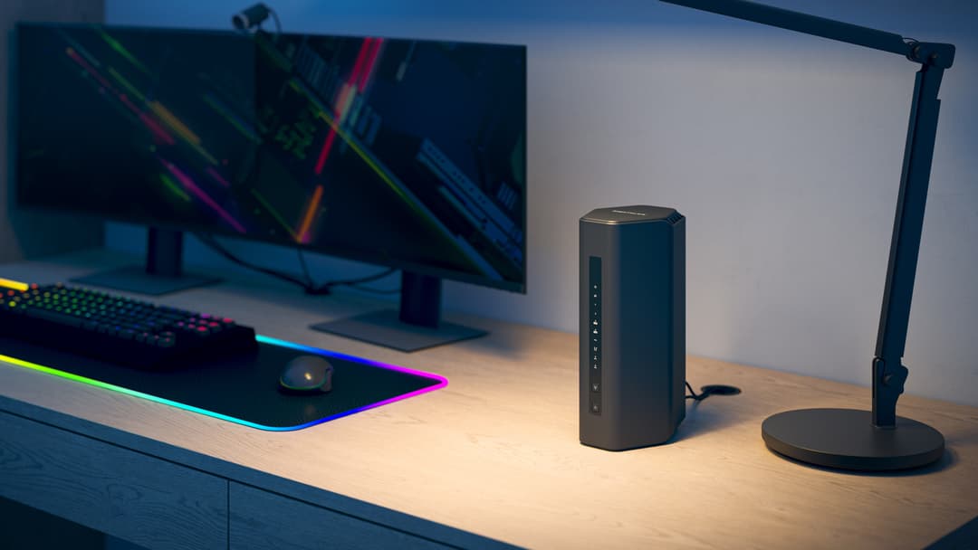 Routeur WiFi 7 Nighthawk RS300 noir cylindrique posé sur un bureau avec écran et clavier RGB en arrière-plan
