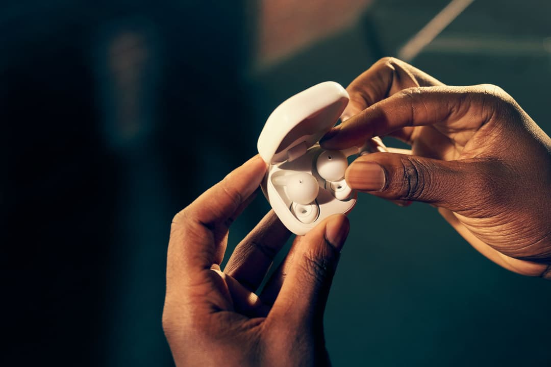 Deux mains tenant un étui blanc ouvert contenant des écouteurs sans fil Sony LinkBuds blancs