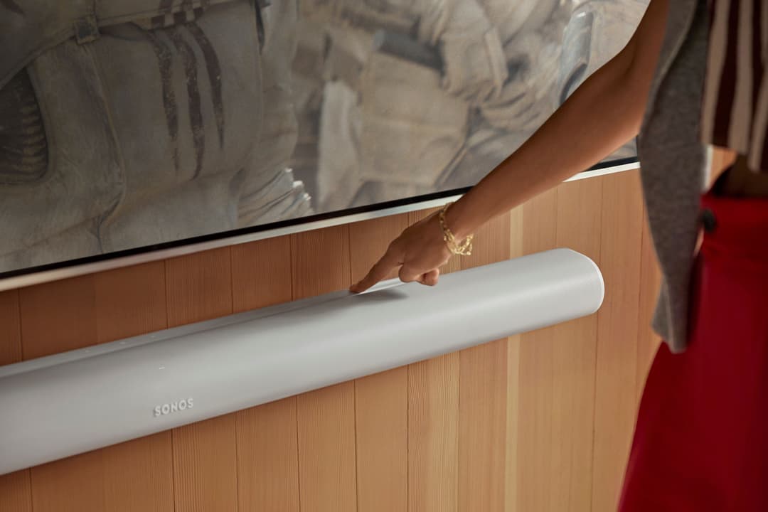 Barre de son Sonos Arc Ultra blanche installée sous un téléviseur, main la touchant