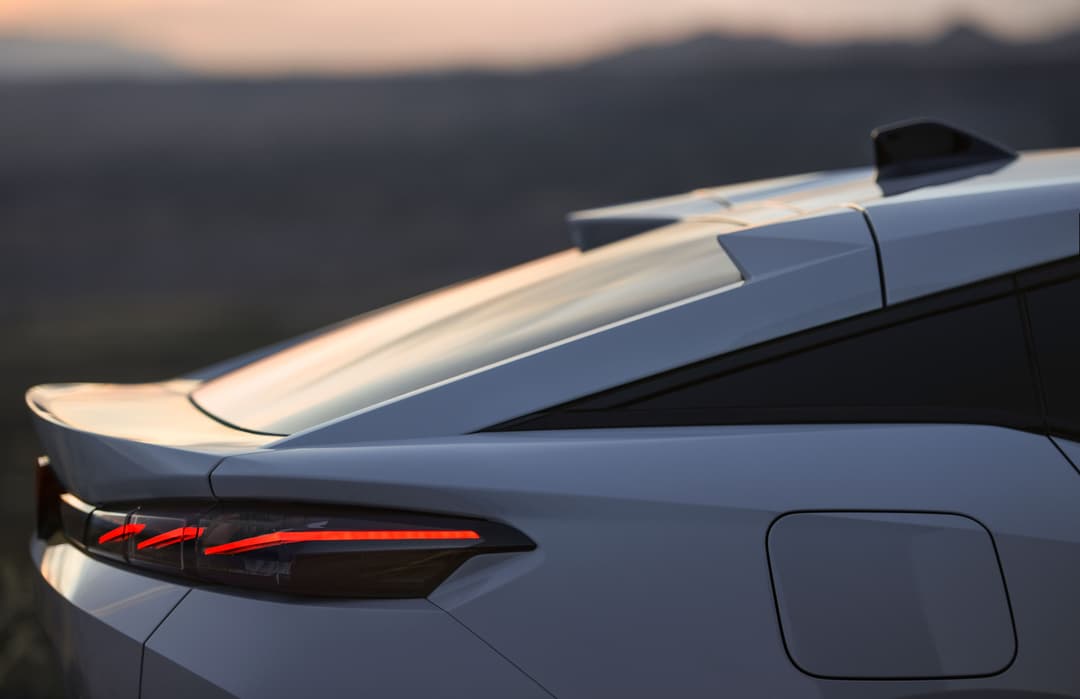 Peugeot E-408 blanche de profil, détail du coffre ouvert et du feu arrière rouge en lumière dorée