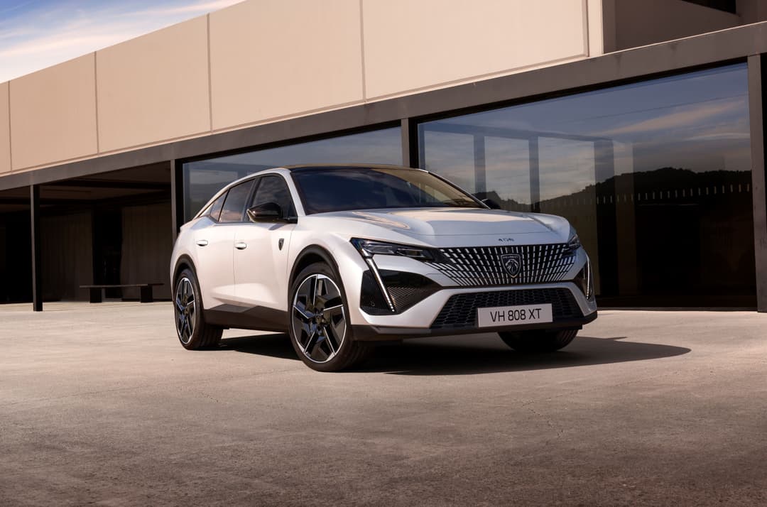 Peugeot E-408 blanc de profil, SUV électrique au design épuré avec phares effilés et grille spécifique, garé devant bâtiment moderne
