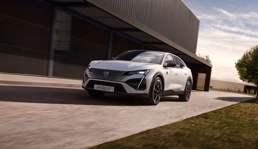 Peugeot E-408 blanche garée devant un bâtiment industriel, vue de trois quarts