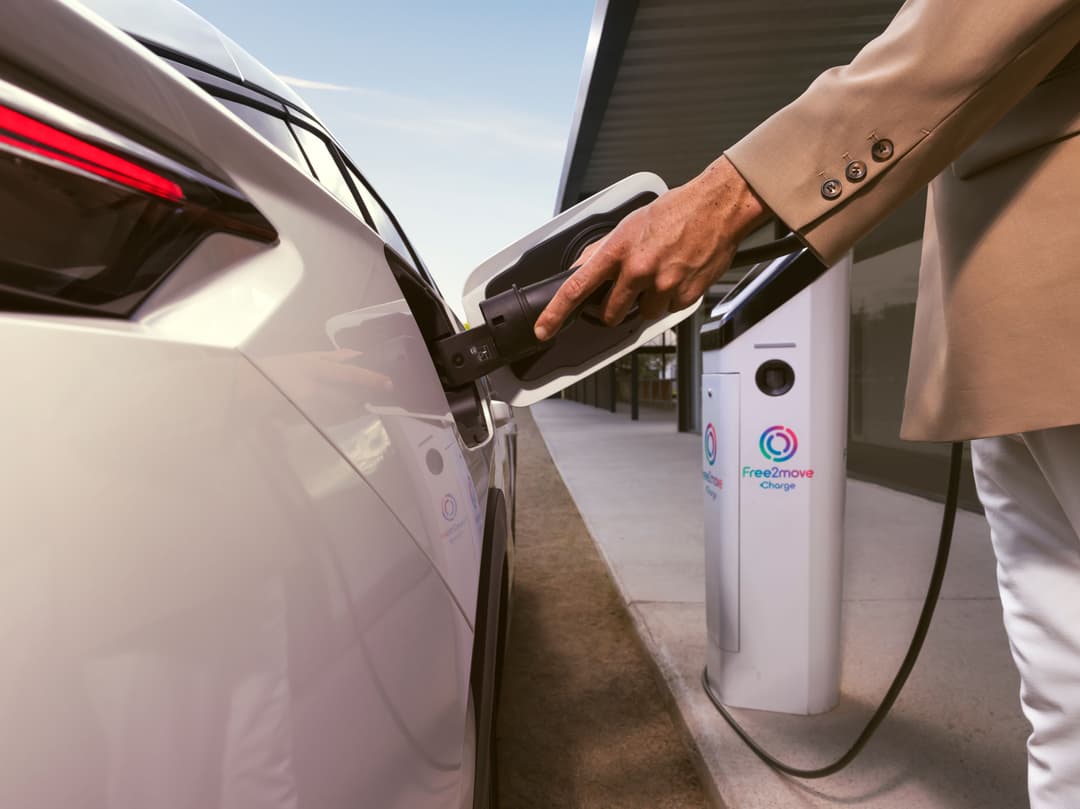 Peugeot E-408 blanche en recharge sur une borne Free2move, main tenant le pistolet de charge