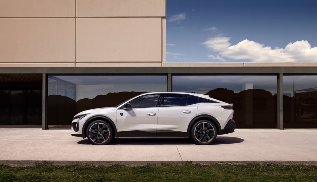 Peugeot E-408 blanche de profil, garée devant un bâtiment moderne aux baies vitrées, sous ciel dégagé