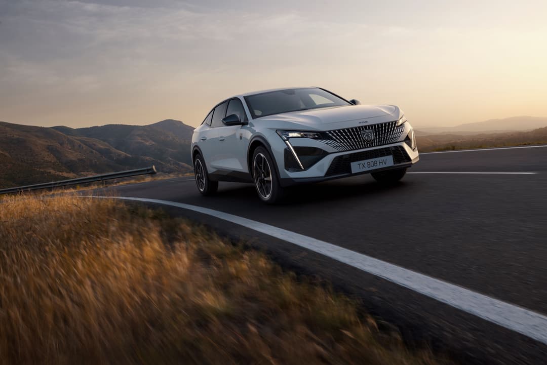 Peugeot E-408 blanche circulant sur une route de montagne au coucher du soleil, avec paysage aride en arrière-plan