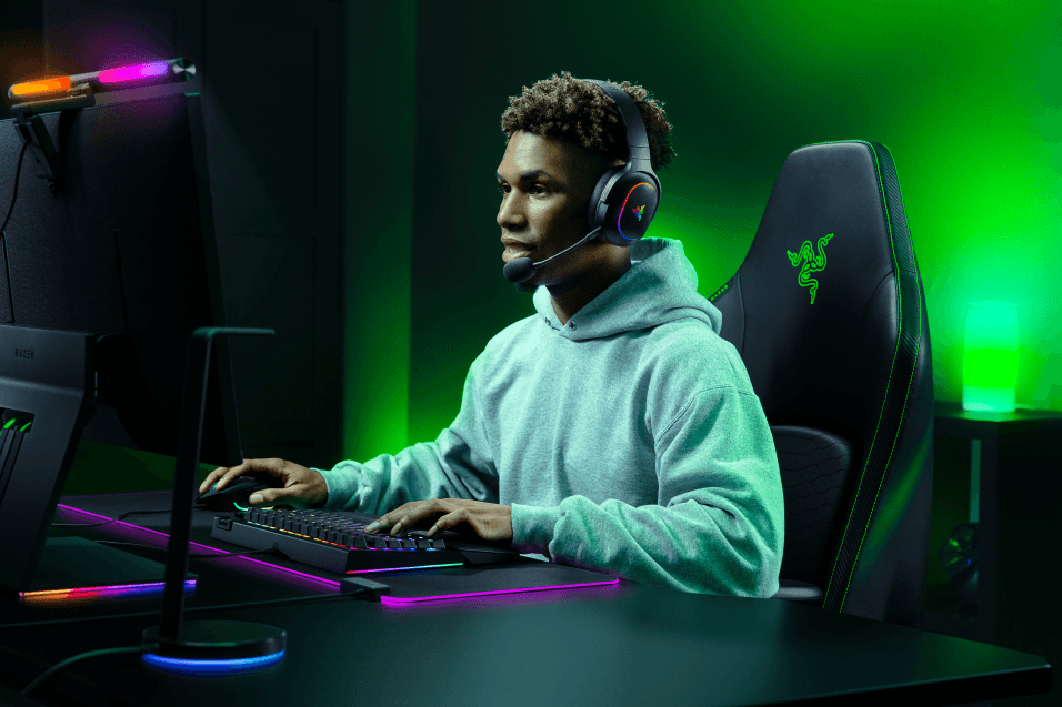 Gamer portant un casque Razer Barracuda X Chroma devant un bureau gaming illuminé de néon vert et rose