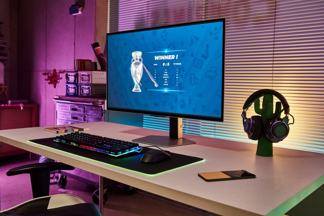 Bureau gaming avec écran affichant un écran de victoire, clavier rétroéclairé, casque sur support, ambiance rose et cyan