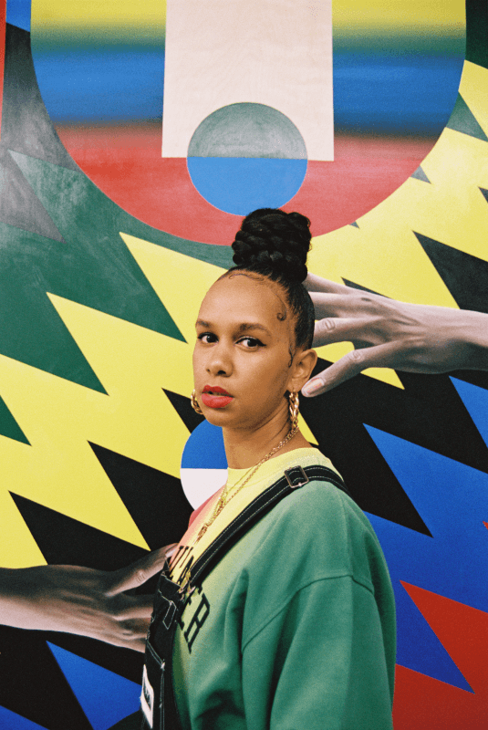 Affiche du Montreux Jazz Festival 59e édition : femme face caméra devant une fresque colorée aux formes géométriques et dégradés de jaune, bleu, rouge et vert