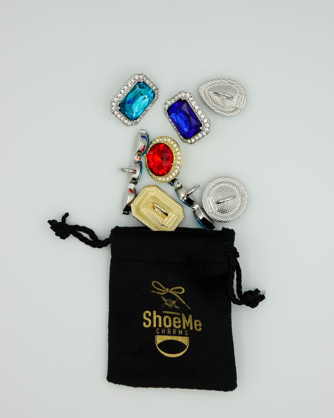 ShoeMe Charms : collection de bijoux pour chaussures aux pierres colorées bleue, rouge et dorée sortant d'une pochette noire