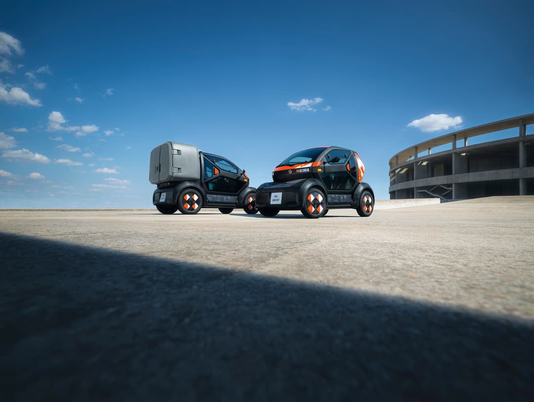 Deux micro-citadines Mobilize Duo et Bento blanches et oranges avec portes papillon ouvertes sur un parking couvert