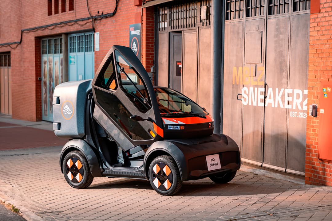Mobilize Duo, micro-citadine électrique noire et orange avec portes papillon ouvertes, stationnée dans une rue urbaine en briques rouges