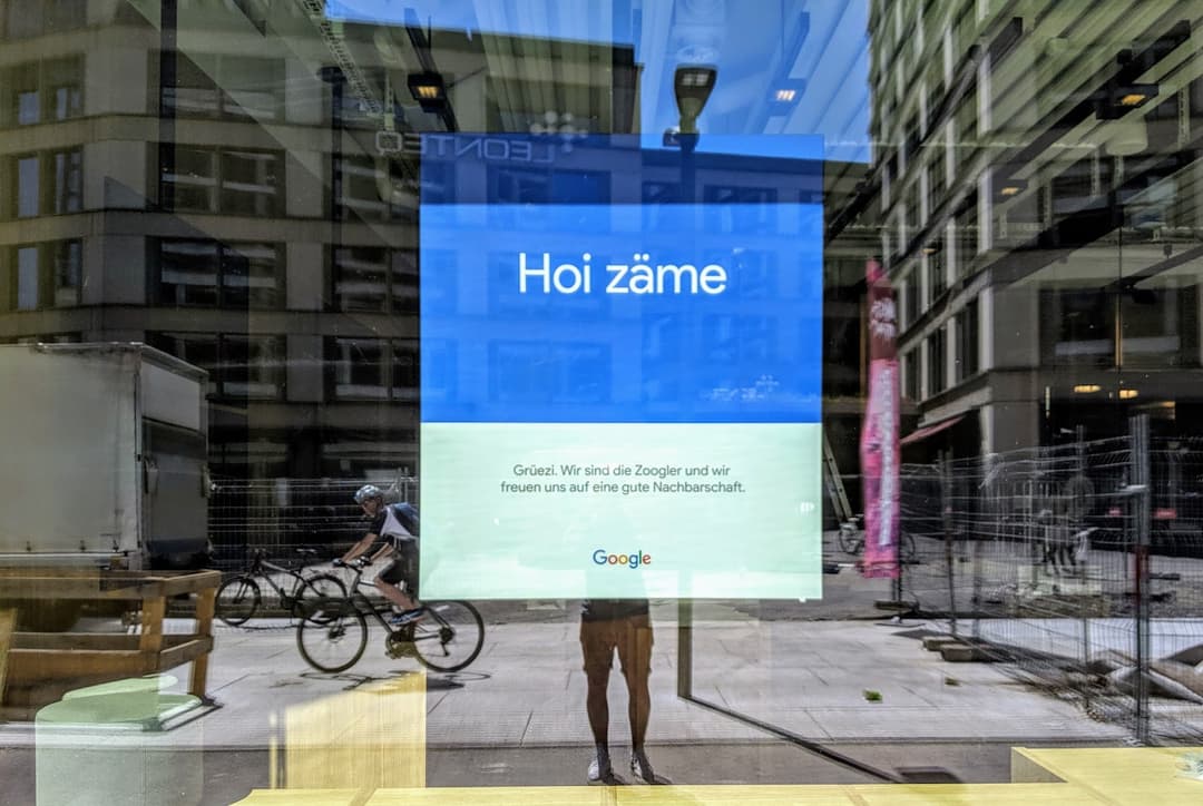 Affiche Google dans une rue de Zurich avec le texte « Hoi zäme » sur fond bleu et vert, devant immeubles urbains