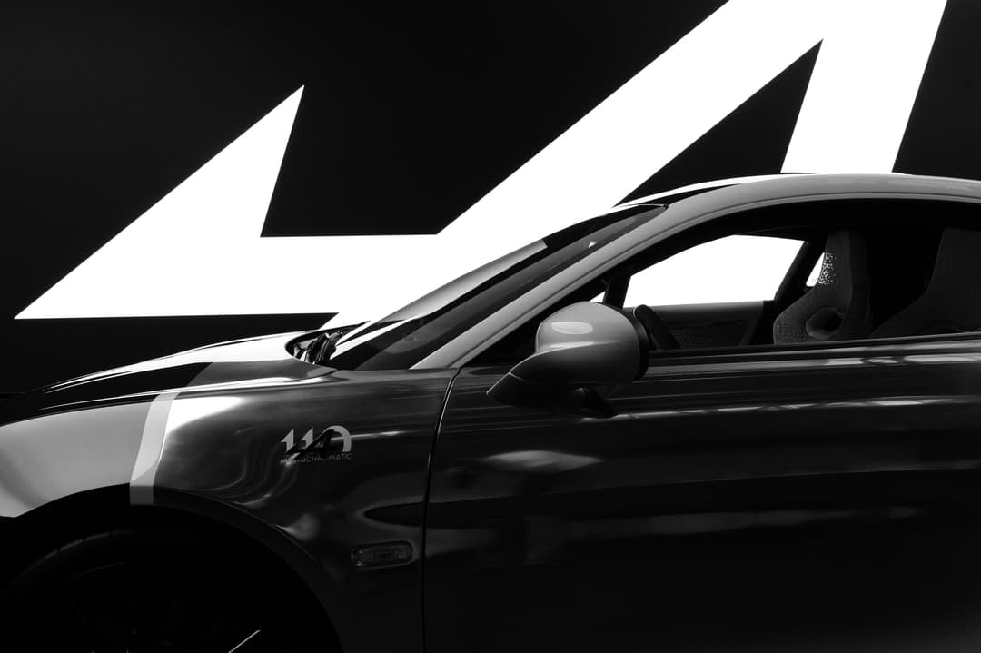 Alpine A110 S en noir et blanc, carrosserie illuminée par des contrastes d'ombre et de lumière, motifs géométriques blancs en arrière-plan