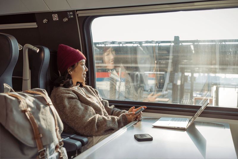 Femme en bonnet rouge dans un bus avec un routeur mobile Nighthawk M3 sur une table, tenant un smartphone
