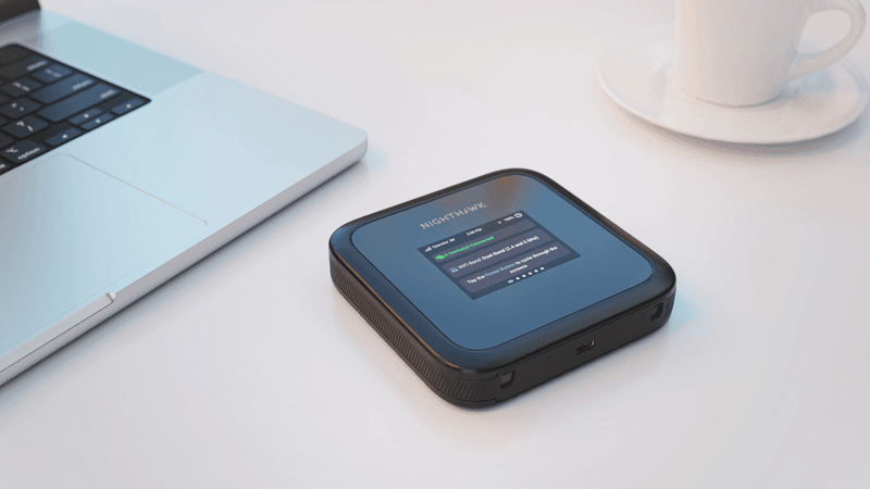 Routeur mobile NETGEAR Nighthawk M3 noir et bleu sur un bureau blanc, à côté d'un ordinateur portable et d'une tasse