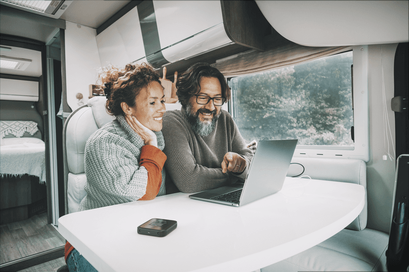 Couple utilisant un laptop à bord d'un camping-car avec vue forêt, routeur NETGEAR Nighthawk M3 sur table