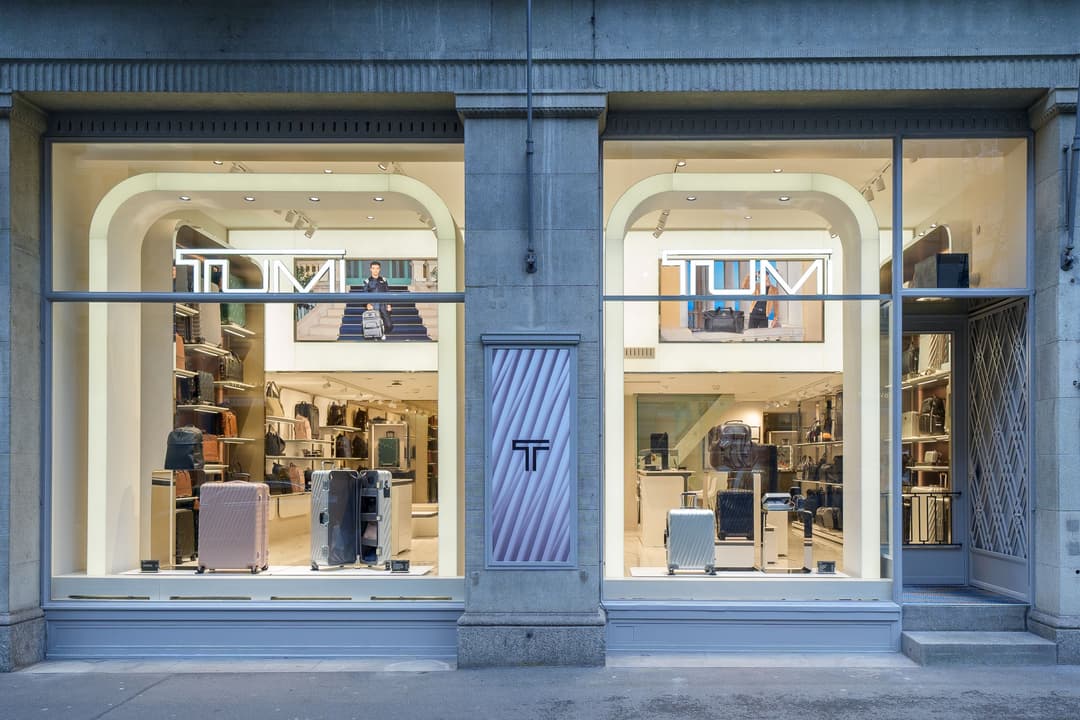 Façade de la boutique TUMI à Zurich avec deux grandes vitrines en arches illuminées, présentant des bagages et valises, séparées par un pilier bleu