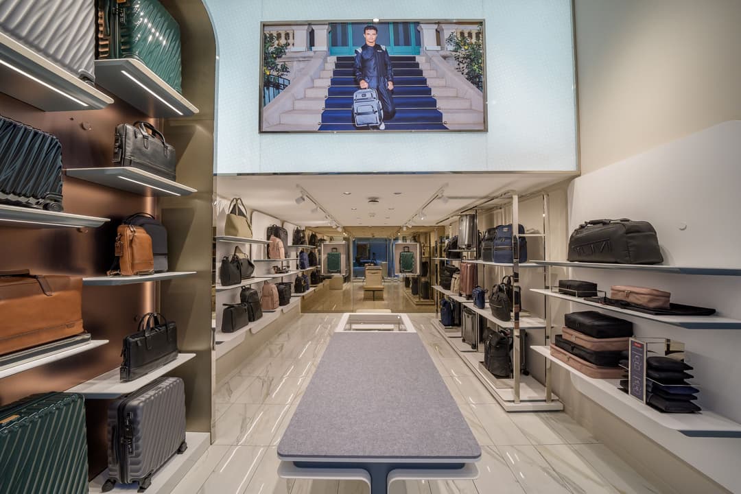 Intérieur de la boutique TUMI à Zurich, avec étagères illuminées présentant des valises et sacs de voyage en cuir et noir, panneaux lumineux et affiche murale montrant un homme avec une valise