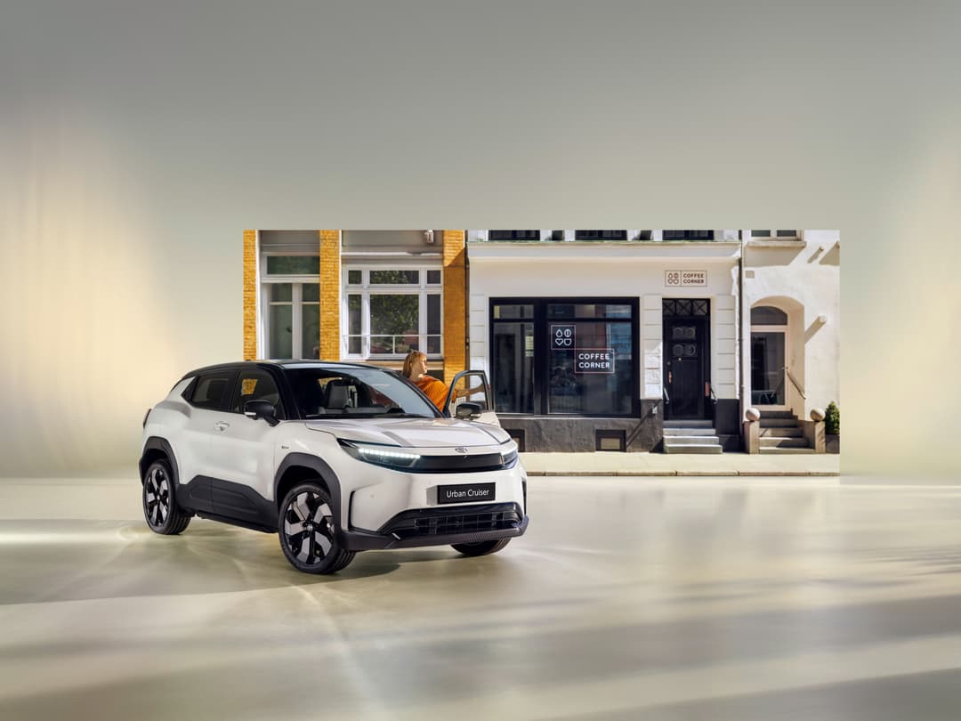 Toyota Urban Cruiser blanc et noir, SUV électrique compact, stationné devant une façade urbaine avec une boutique de café