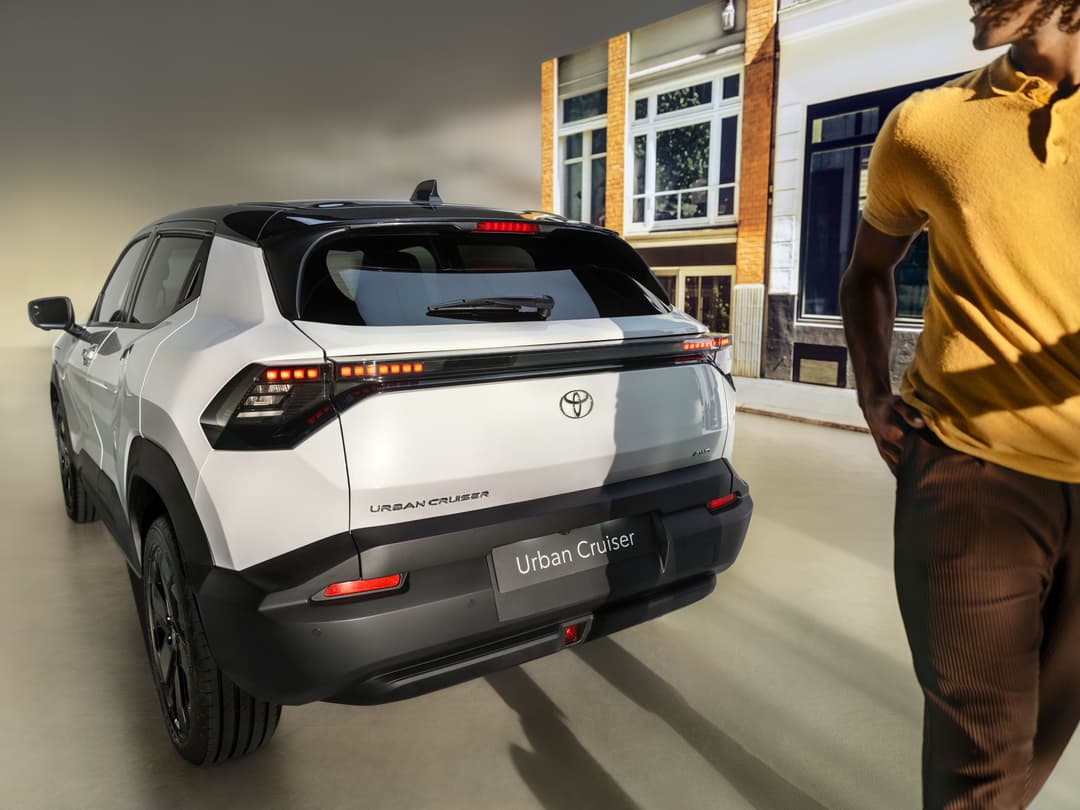 Toyota Urban Cruiser blanc vu de trois quarts arrière, avec feux LED rouges et noirs, stationné devant un bâtiment en briques