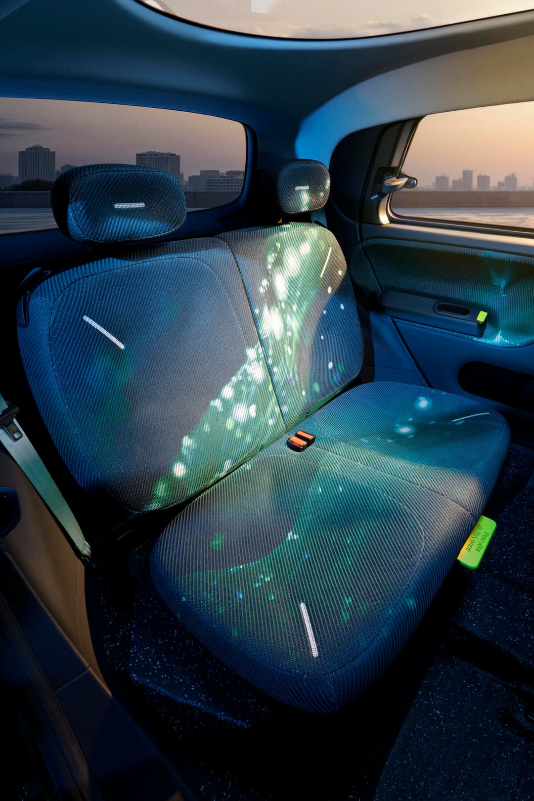 Intérieur de la Renault Twingo E-Tech avec sièges bleus à motifs luminescents, espace de rangement plat et accents verts, vue sur la ville depuis les fenêtres