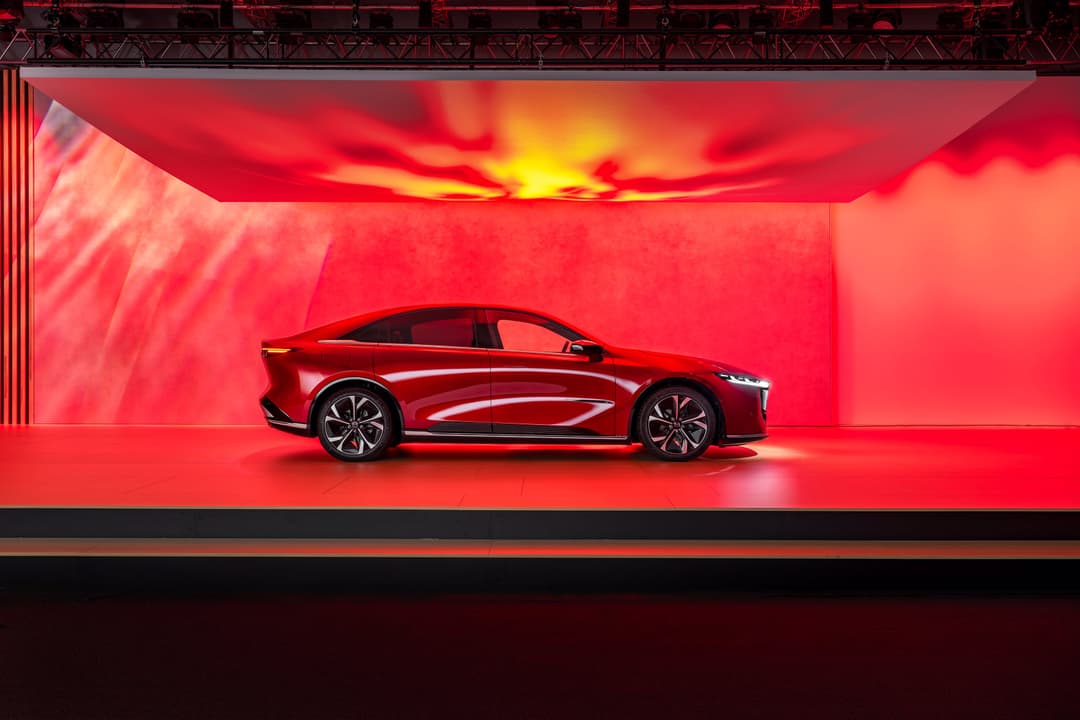 Mazda6e rouge présentée sur un podium illuminé d'une lumière rouge et orange intense
