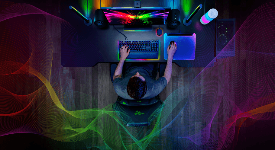 Joueur à son bureau de gaming Razer vu de haut, avec écran, clavier et souris RGB illuminés de couleurs vives