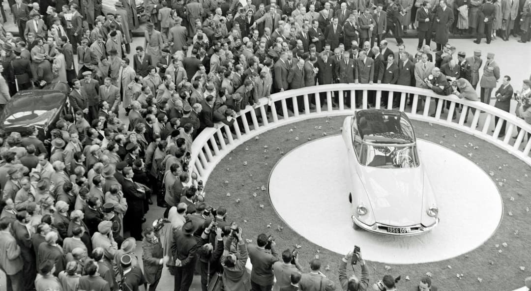 DS 19 au centre d'une plateforme circulaire entourée de centaines de visiteurs lors de sa présentation au Salon de l'automobile