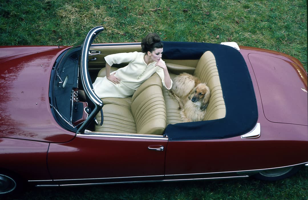 DS Cabriolet rouge bordeaux, toit ouvert, avec une femme et un chien dans l'habitacle en cuir beige
