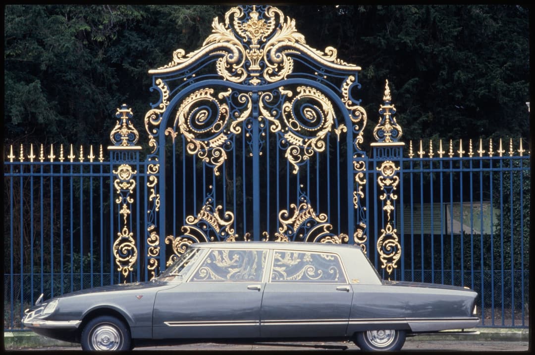 DS présidentielle allongée de couleur grise garée devant un portail bleu et or aux ornements baroques