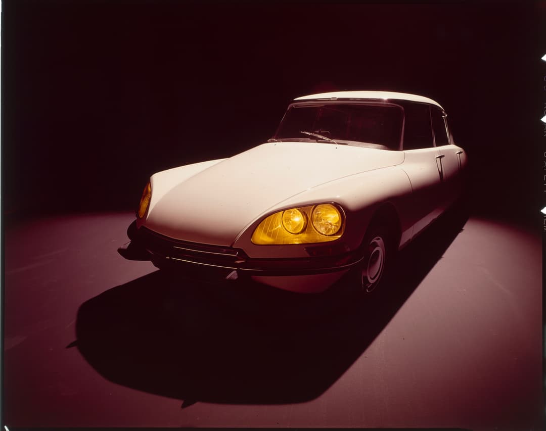 Citroën DS des années 1960, bicouleur beige et bordeaux, phares jaunes allumés, photographiée sur fond noir