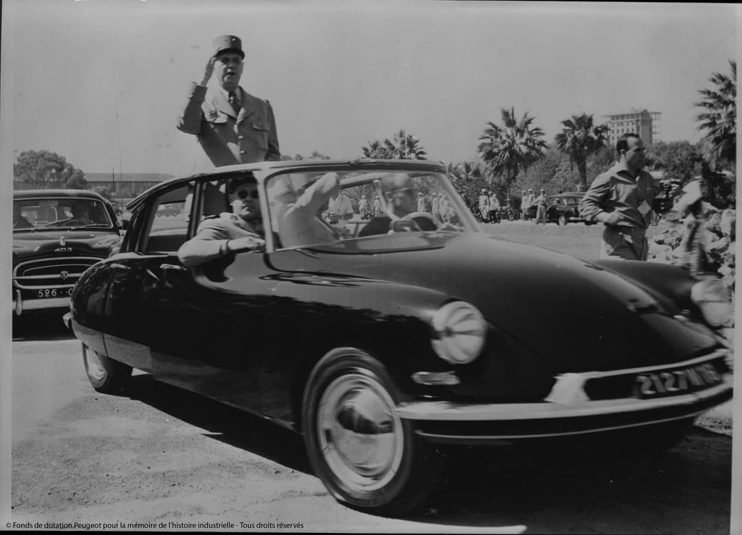 Citroën DS des années 1950, voiture noire aux formes épurées, présentée lors d'un événement public avec palmiers en arrière-plan