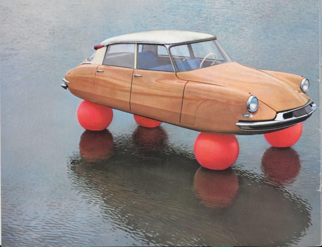Citroën DS beige soulevée par quatre boules rouges gonflables, démontrant sa suspension hydropneumatique révolutionnaire