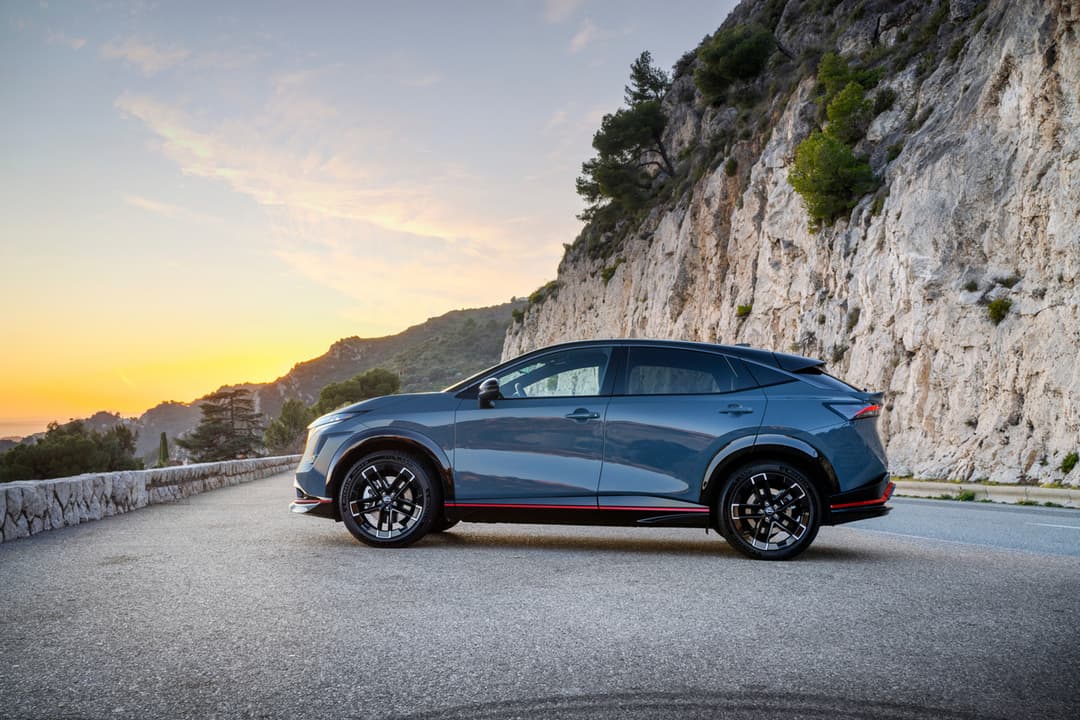 Nissan ARIYA NISMO bleu garé de profil sur une route côtière avec falaise blanche et coucher de soleil