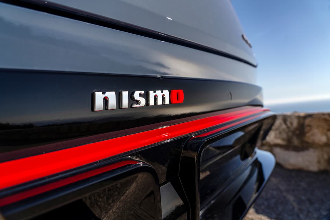 Badge NISMO en relief sur la carrosserie grise et noire du Nissan ARIYA, avec une bande rouge distinctive sur le flanc