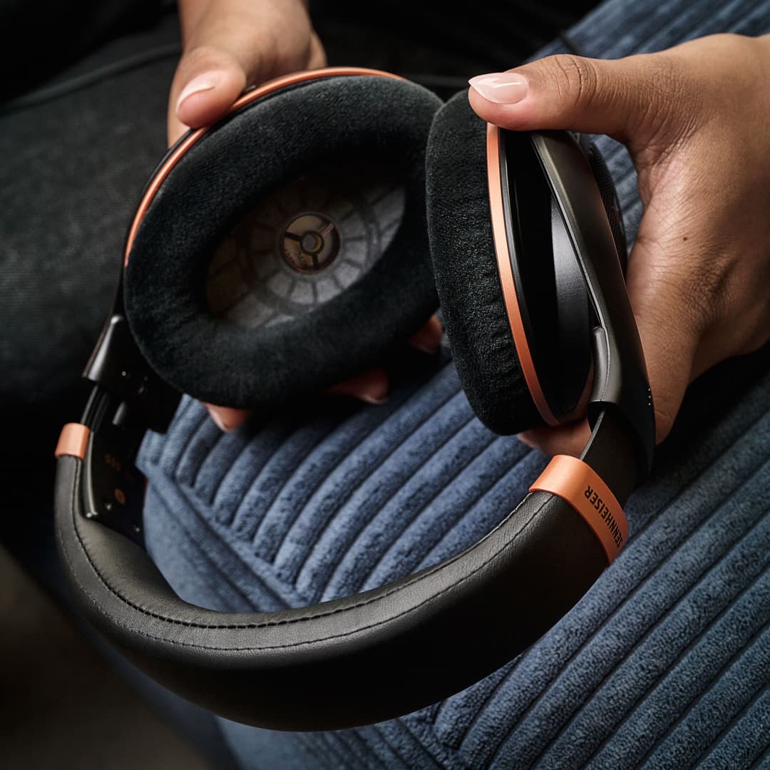 Casque HD 505 aux écoutilles détachables, arceau orange et noir, tenu entre les mains au-dessus d'un pull bleu