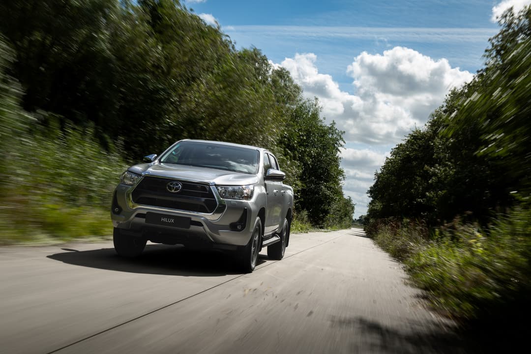 Toyota Hilux blanc roulant sur une route de campagne bordée de végétation luxuriante