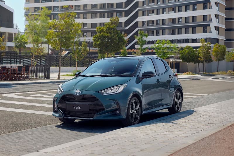 Toyota Yaris bleu-gris stationnée sur un parking urbain, immeubles résidentiels en arrière-plan