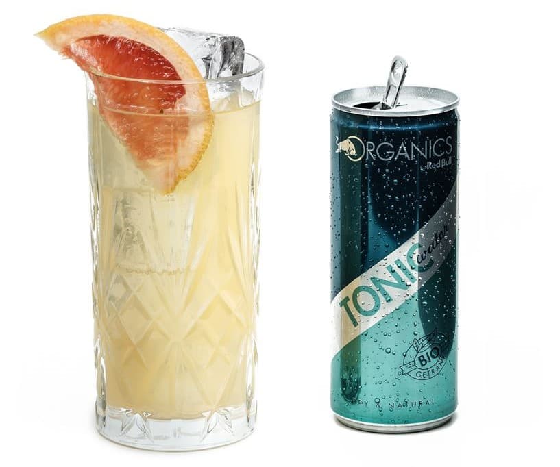 Verre de cocktail jaune pâle avec glaçons et tranche de pamplemousse, canette ORGANICS Tonic by Red Bull vert foncé