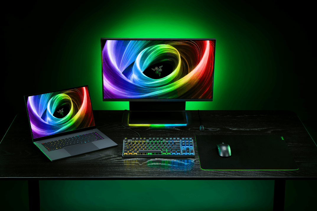 Razer Blade 18 ouvert sur un bureau aux côtés d'un écran, d'un clavier et d'une souris Razer, tous éclairés en vert fluo
