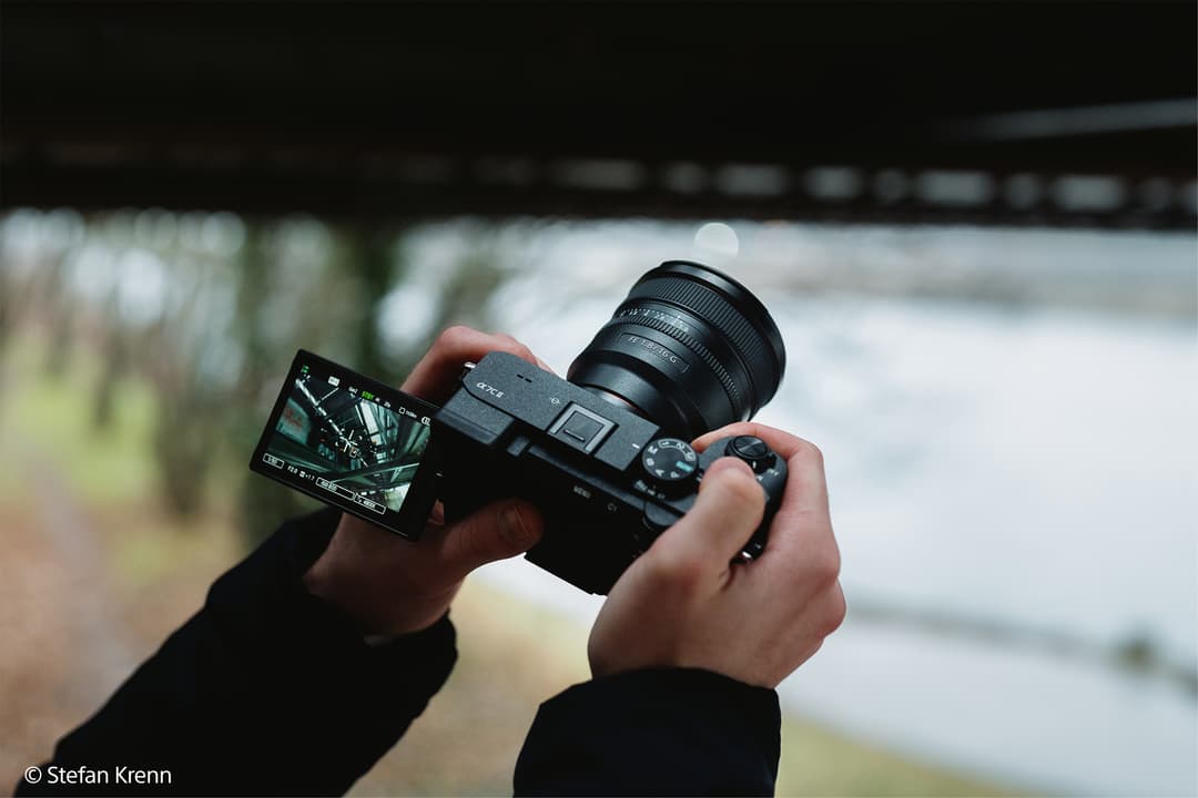 Boîtier Sony Alpha noir avec nouvel objectif grand-angle fixe tenu en mains devant un paysage flou