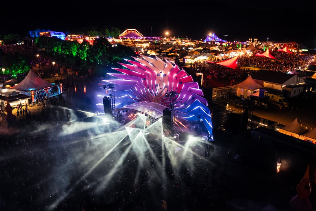 Scène du Paléo Festival Nyon de nuit, illuminée par des projecteurs blancs et une structure décorée de néons roses et bleus