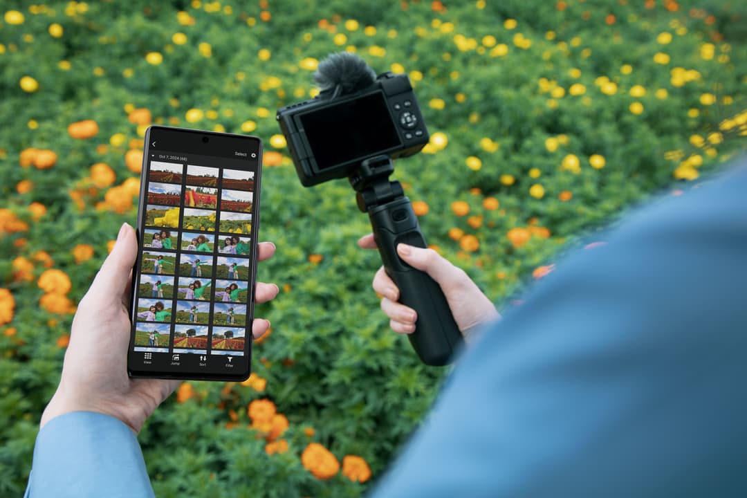 Caméra Canon noire montée sur stabilisateur avec microphone, contrôlée via smartphone affichant la galerie vidéo, en extérieur floral