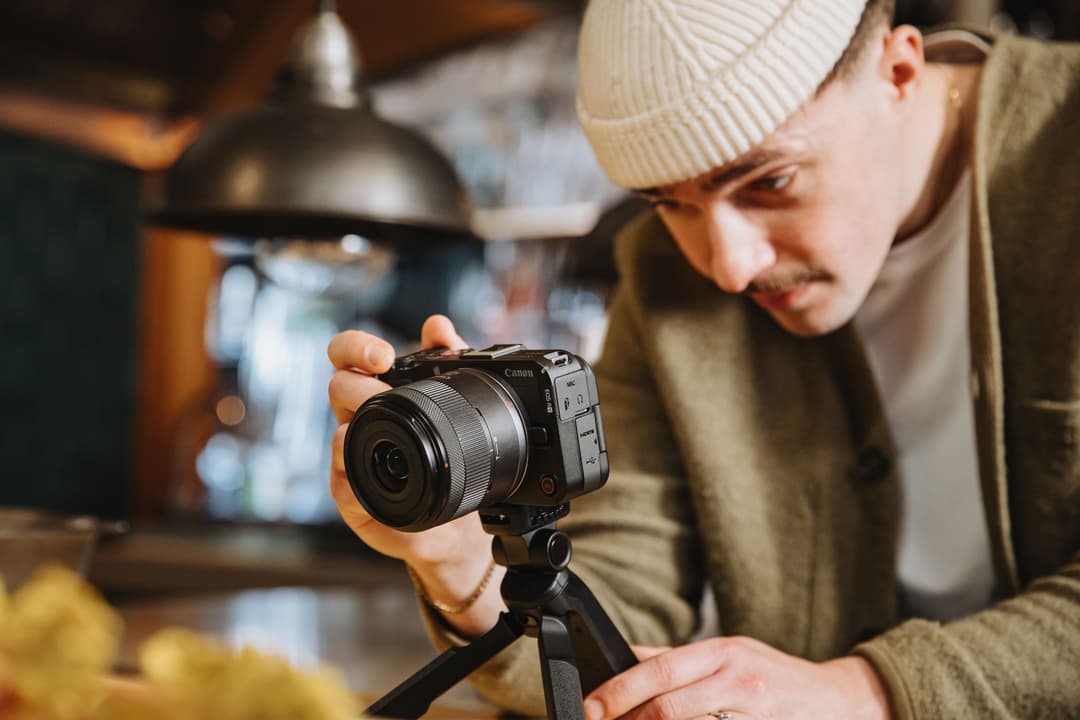 Créateur tenant un appareil photo Canon EOS R50 V équipé d'un objectif, monté sur un trépied en studio